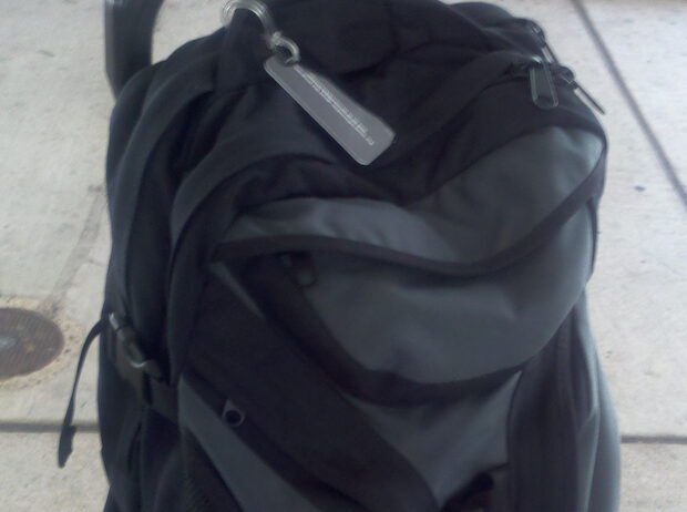 a backpack sitting on a roller suitcase with a visible luggage tag